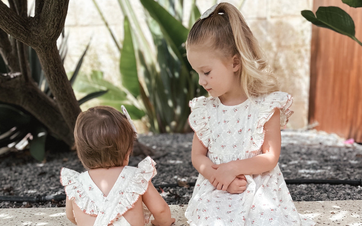 Two young girls in cream floral hand-smocked dress and romper, outdoors