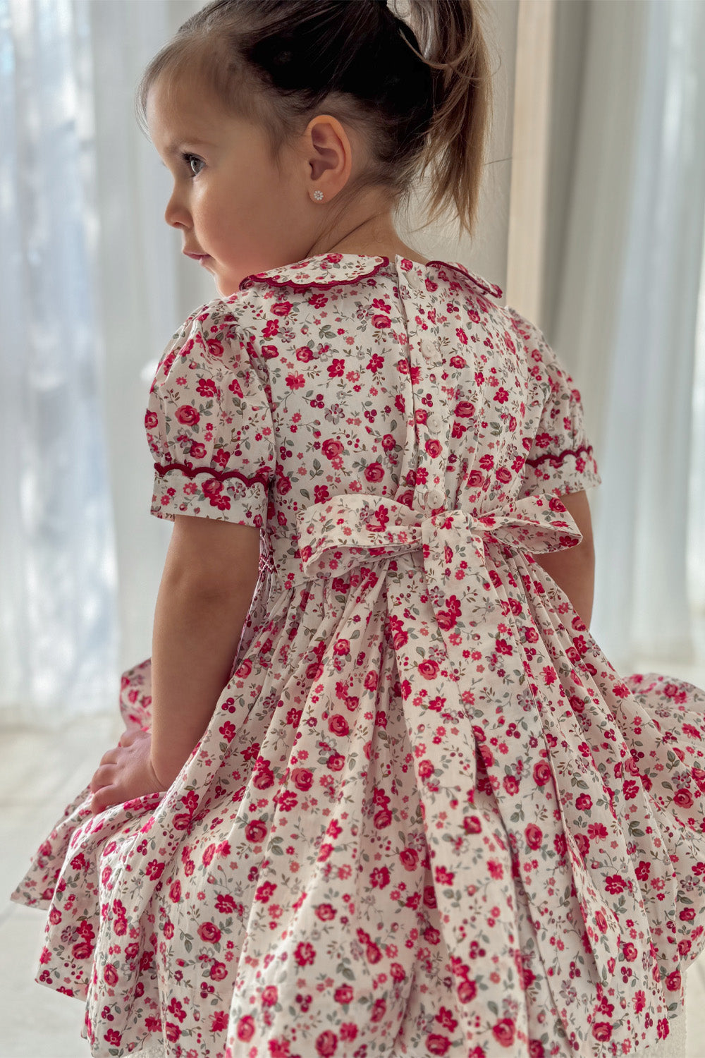 Side back view of cherry red floral girls Christmas dress with scalloped collar and full skirt