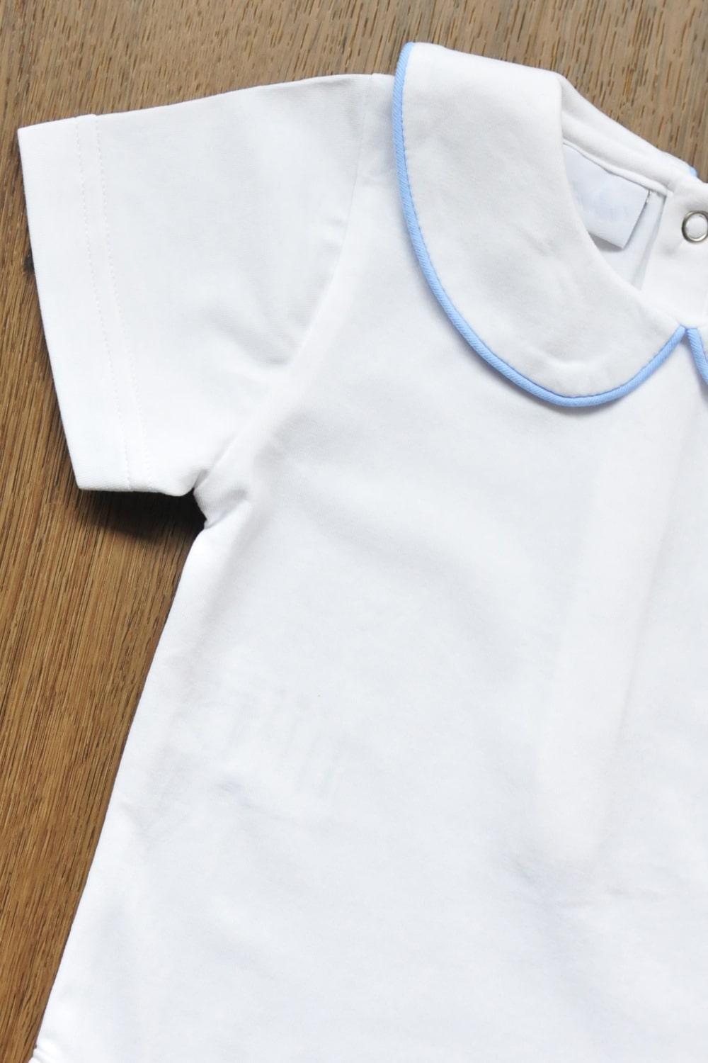 Close-up of Peter Pan collar with pale blue piping on white baby bodysuit