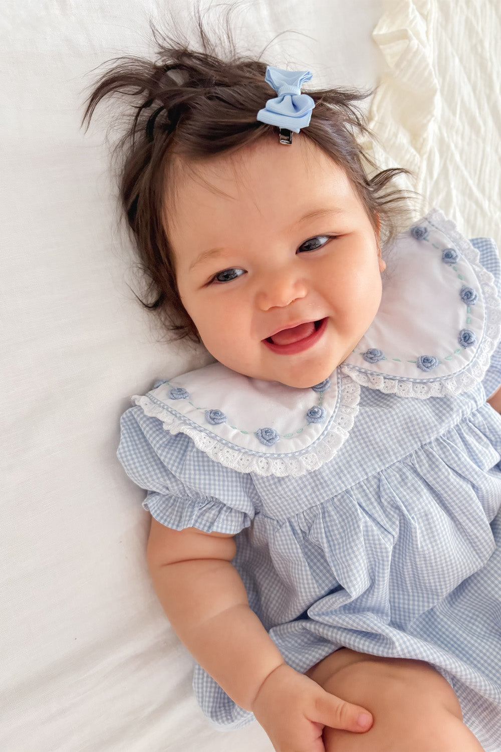 Smiling baby wearing Blue Rosette Gingham Romper with embroidered Peter Pan collar