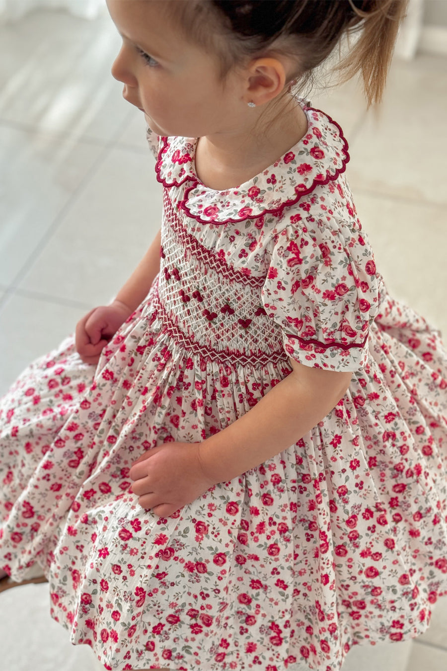 Girl wearing cherry red floral hand smocked dress