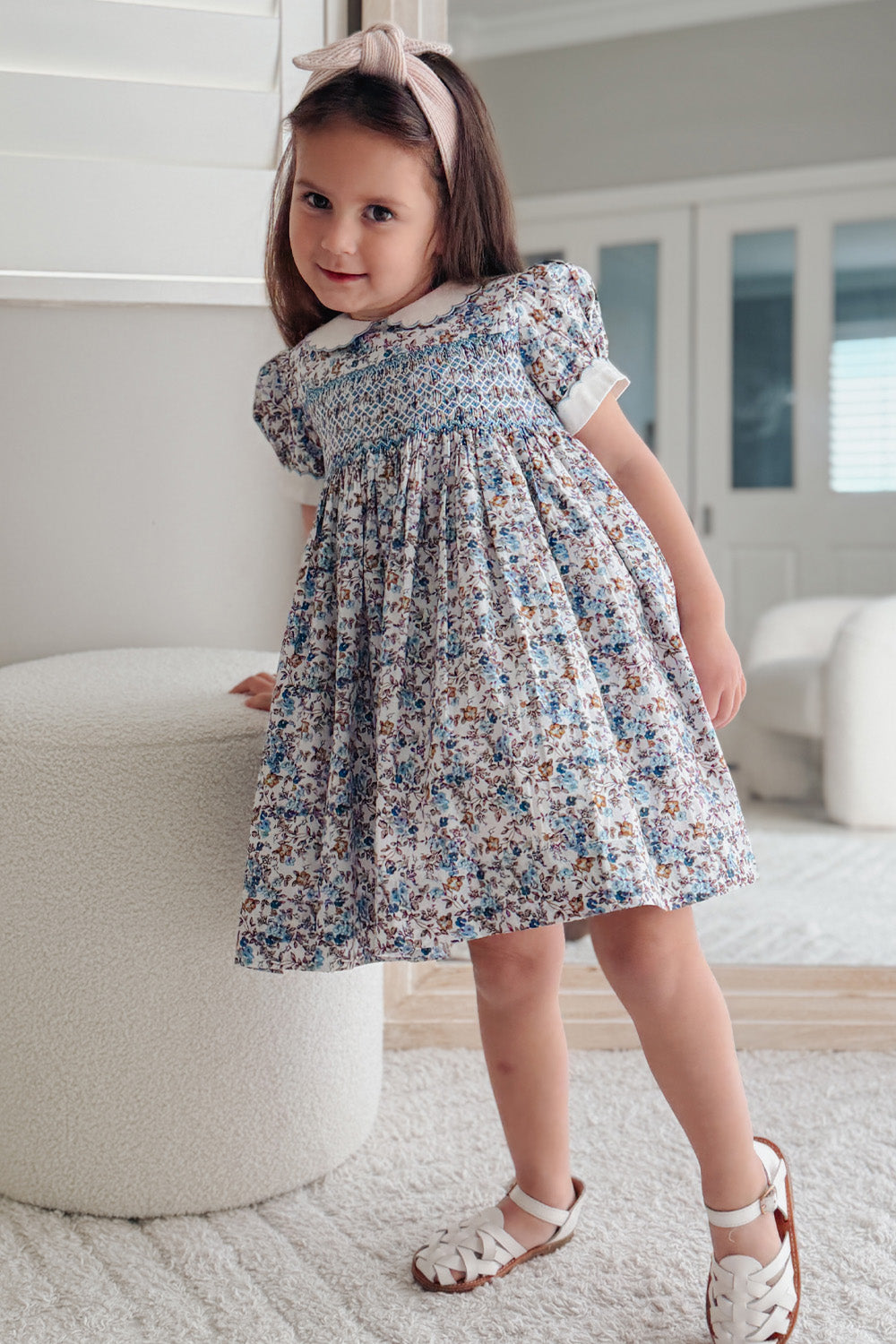 Toddler girl wearing blue floral hand smocked dress with Peter Pan collar and puff sleeves